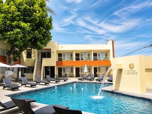 A hotel with a swimming pool, lounge chairs, and umbrellas. - Hotel Cortez Baja Inn – Ensenada (Ensenada)