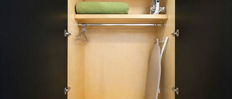 A compact storage unit with a shelf, a hanging rack, and a foldable ironing board.