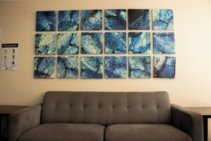 Una sala de estar con un sofá gris y una pared decorada con pinturas abstractas azules.
