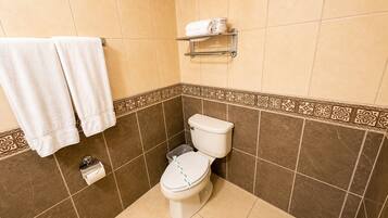 Een badkamer met een toilet, twee handdoeken, een toiletrolhouder en een plankje met een fles.