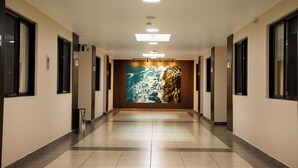 Un couloir d’hôtel avec un sol carrelé, un éclairage encastré et une grande fresque murale représentant une côte rocheuse.