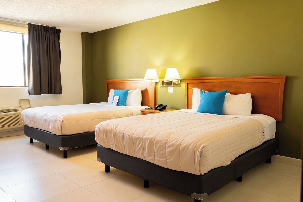 A hotel room with two beds, each with a wooden headboard, white bedding, and blue pillows. There are two bedside lamps and a telephone on the nightstand.