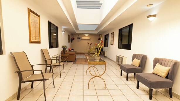 A spacious living area with a high ceiling, a central coffee table, and seating arrangements including chairs and a sofa. - Baja Inn Hoteles La Mesa (Tijuana)