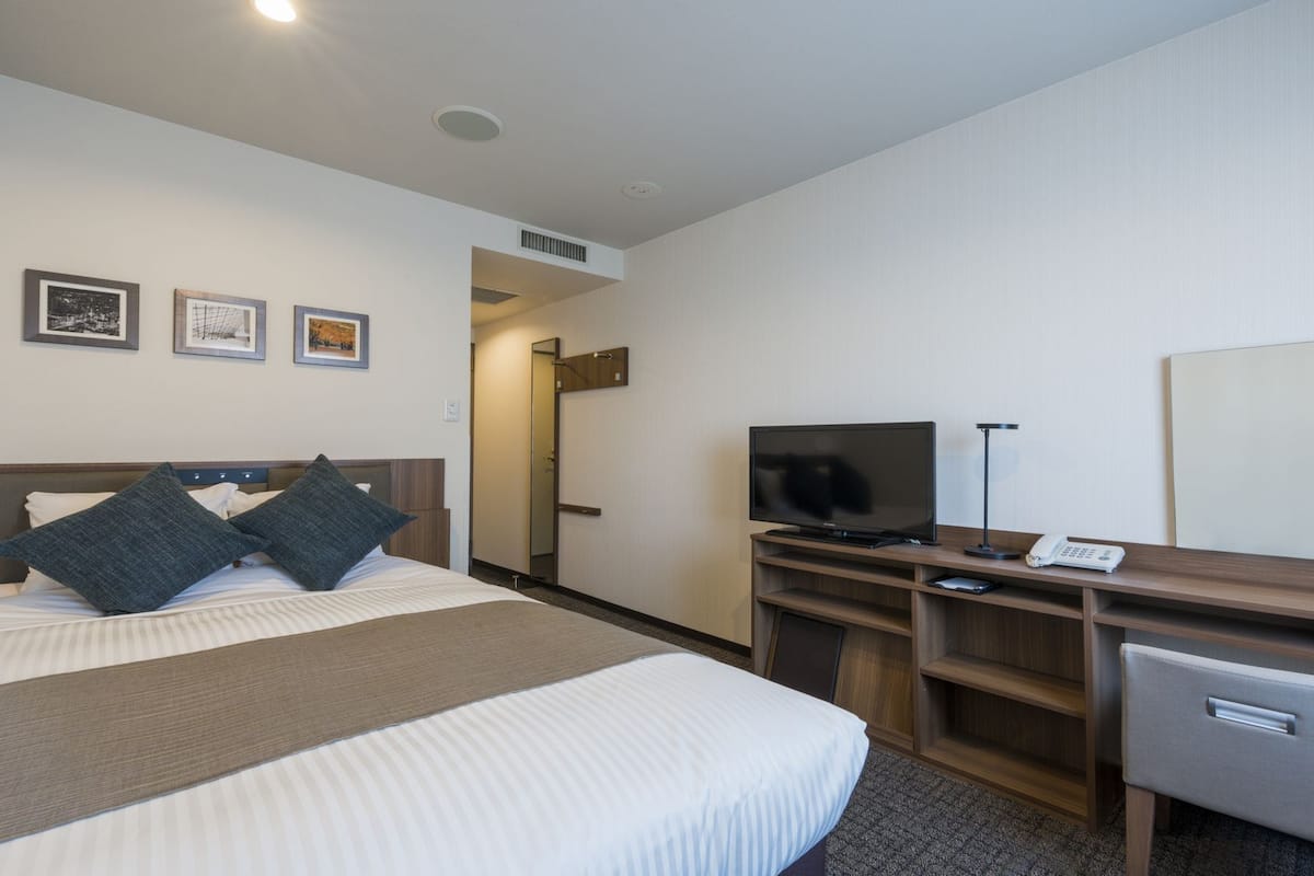 Ein Hotelzimmer mit einem Bett, einem Fernseher, einem Schreibtisch mit Telefon und einem Spiegel.
