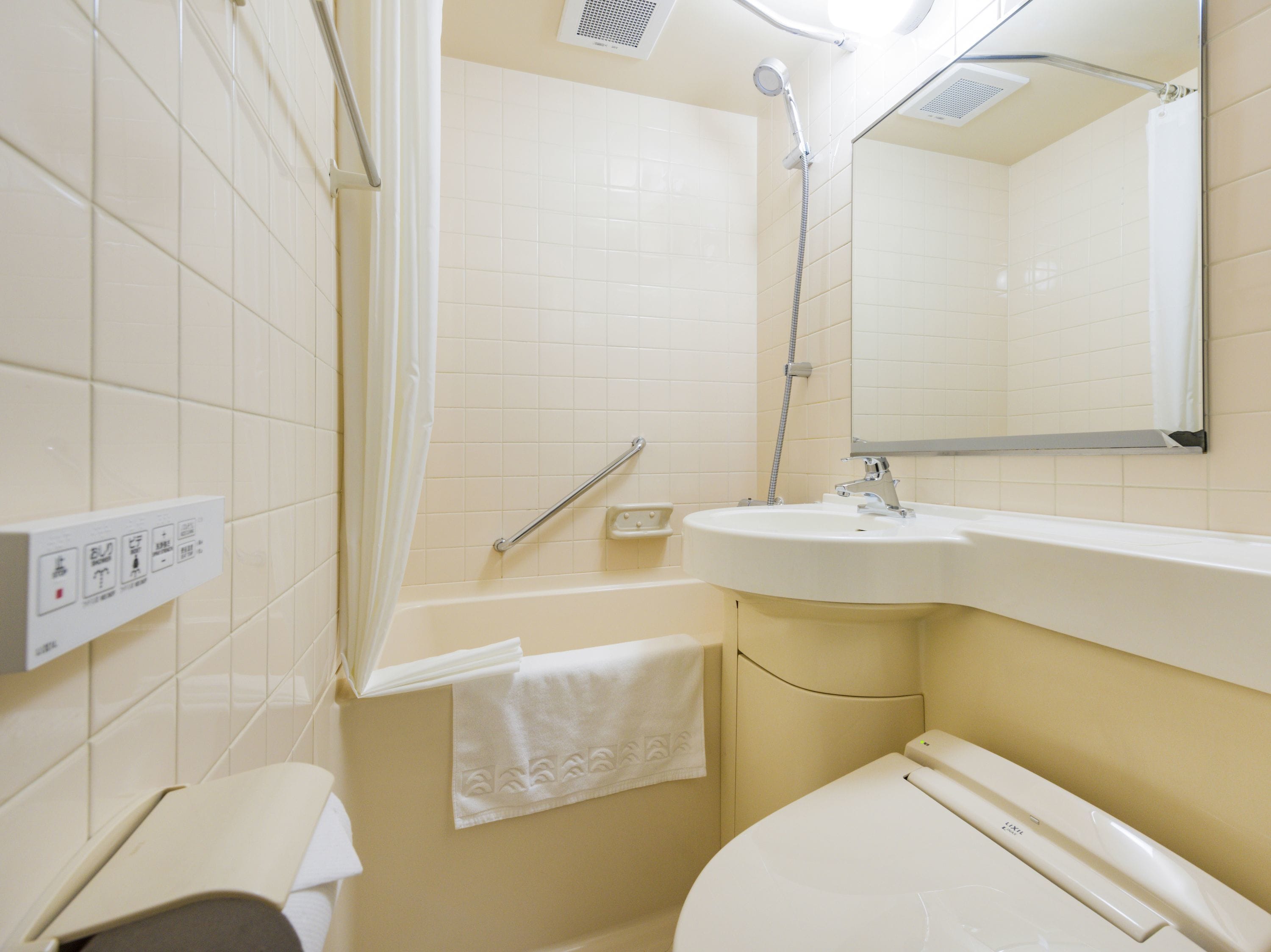 A bathroom with a toilet, sink, shower, and a mirror.