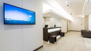 Un área de recepción moderna con un televisor de pantalla plana mostrando un paisaje urbano, una mesa de recepción y un espacio de espera.
