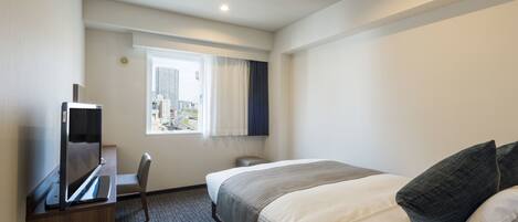 Ein Hotelzimmer mit Bett, Schreibtisch mit Flachbildfernseher, Stuhl, Fenster mit Blick auf die Stadt und Deckenleuchte.