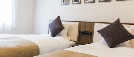 A hotel room with two beds, each with a wooden headboard, white bedding, and dark brown pillows. There are framed pictures on the wall above the beds.