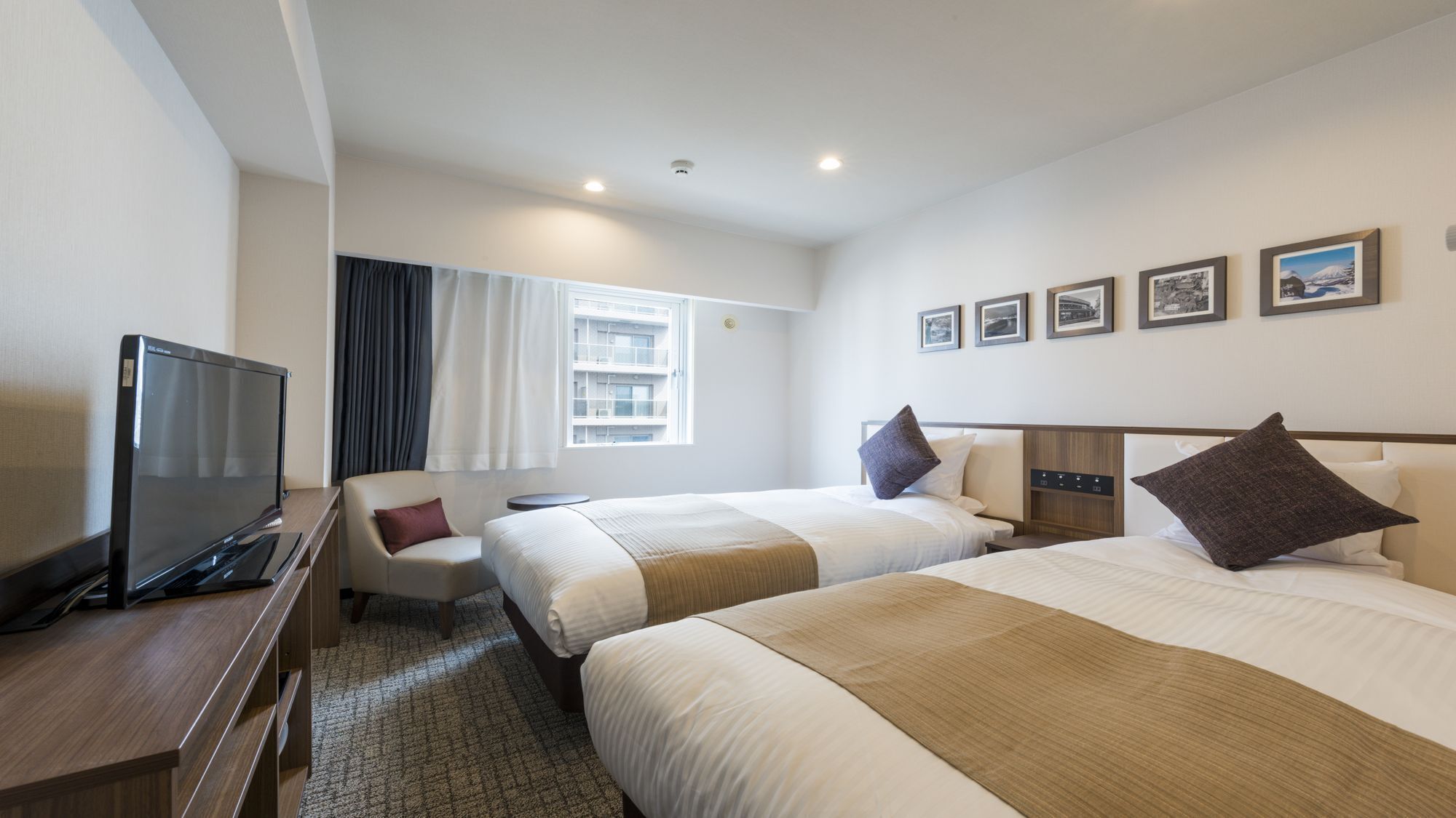 A hotel room with two beds, a TV, a desk, and a window with curtains.