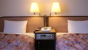 Habitación de hotel con dos camas, cada una con colcha estampada, una mesita de noche entre ellas con lámpara y teléfono, y una lámpara de pared sobre ellas.