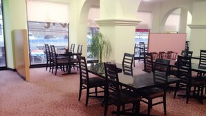 Un salón de conferencias con varias mesas y sillas, ventanas amplias con vistas a un estacionamiento y una alfombra estampada.