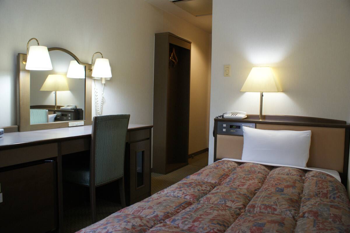 A hotel room with a bed, a desk, a chair, a telephone, and a mirror.