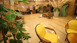 Un hall de hotel con sillas amarillas, un mostrador de recepción y plantas en macetas grandes.