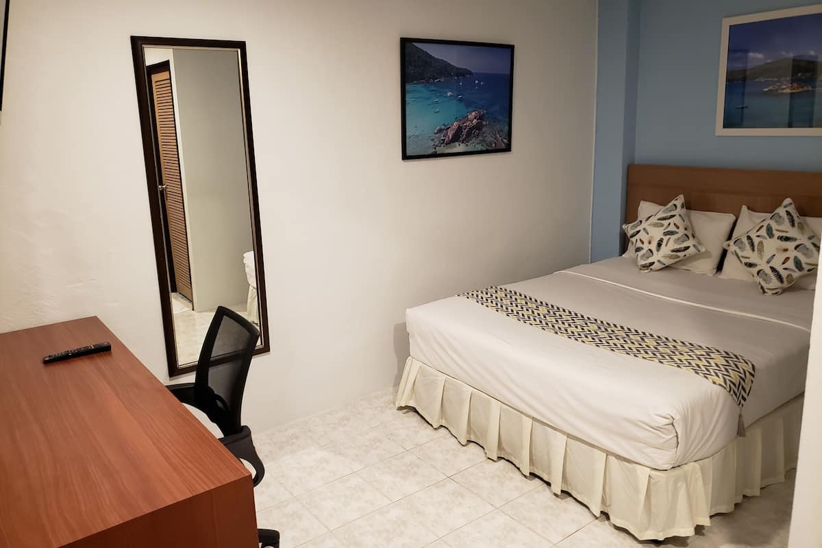 A bedroom with a bed, a desk, a chair, a mirror, and two framed pictures on the wall.