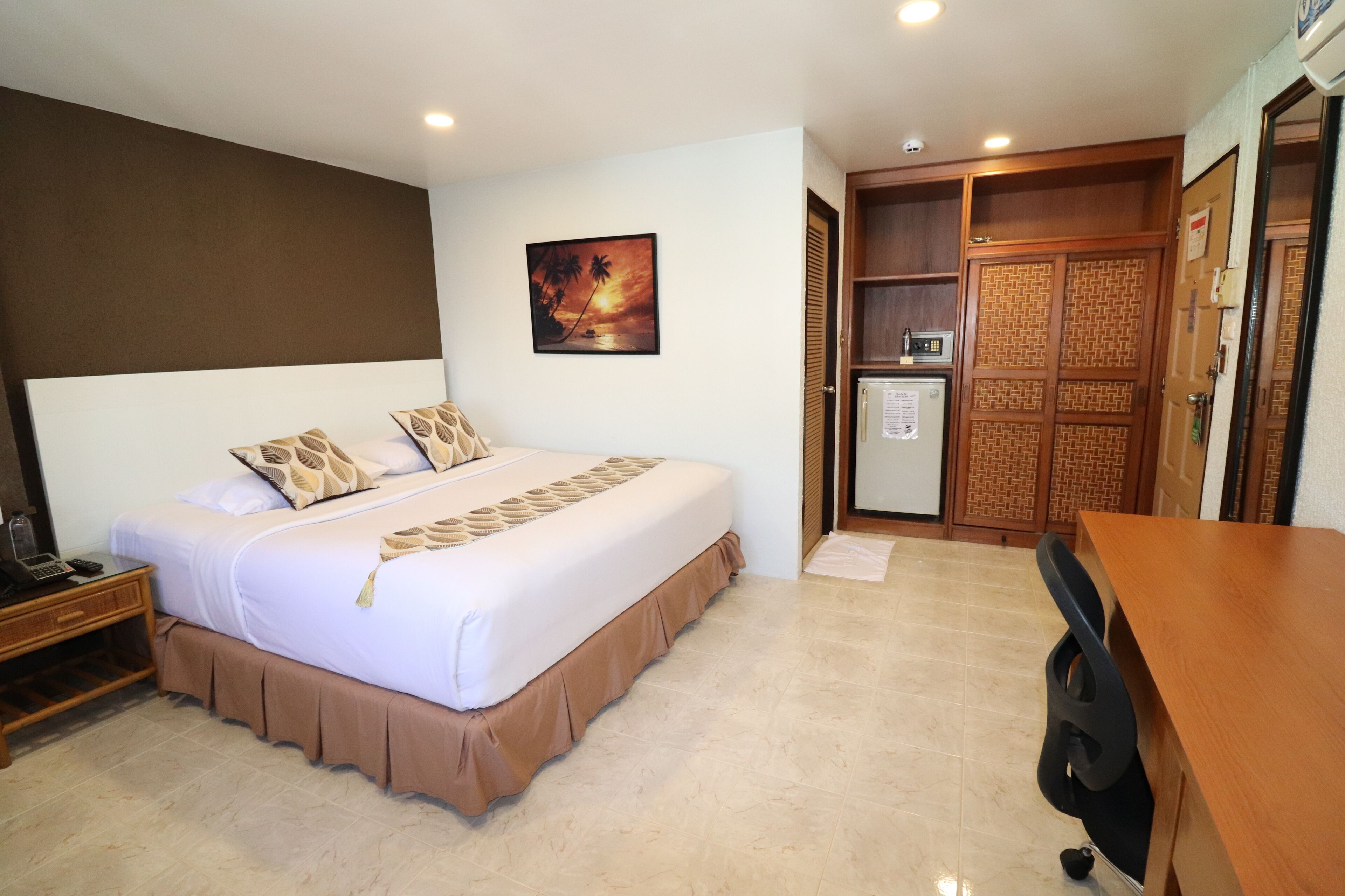 Una habitación de hotel con una cama grande, un escritorio, un armario y un refrigerador pequeño.