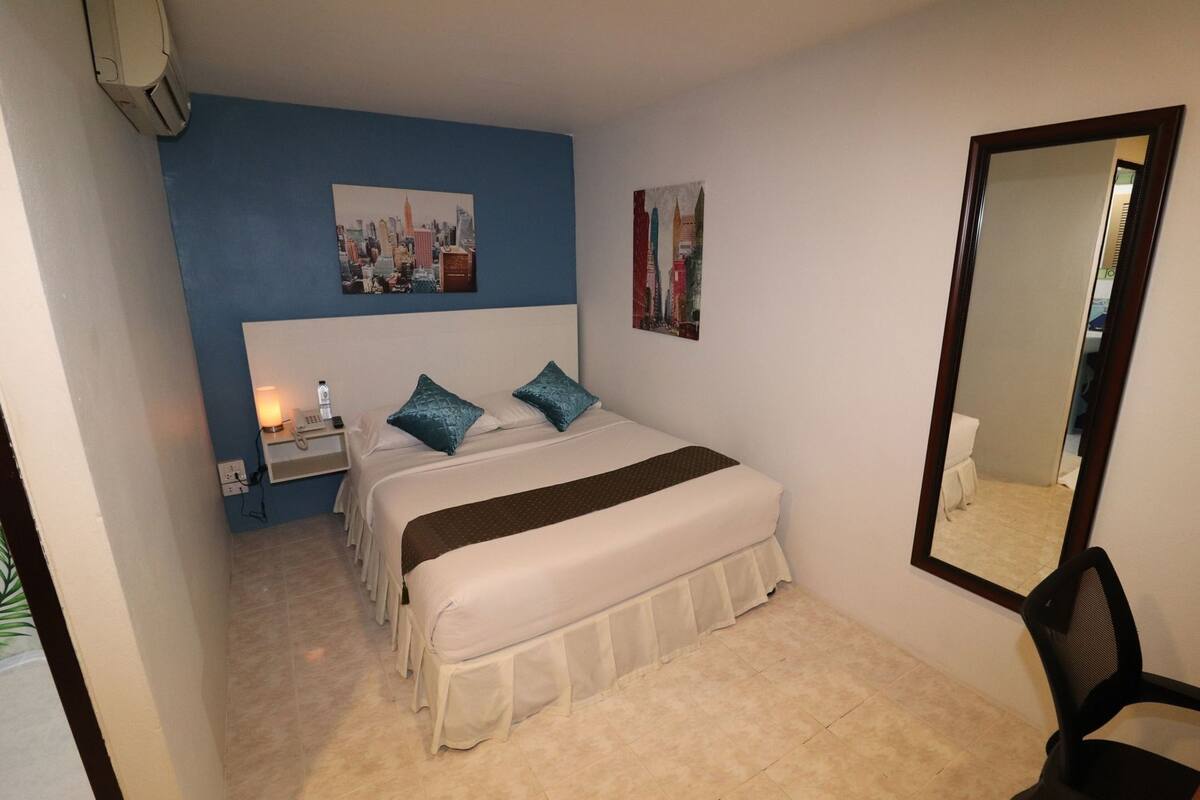 A hotel room with a bed, a nightstand, a mirror, and two paintings on the wall.