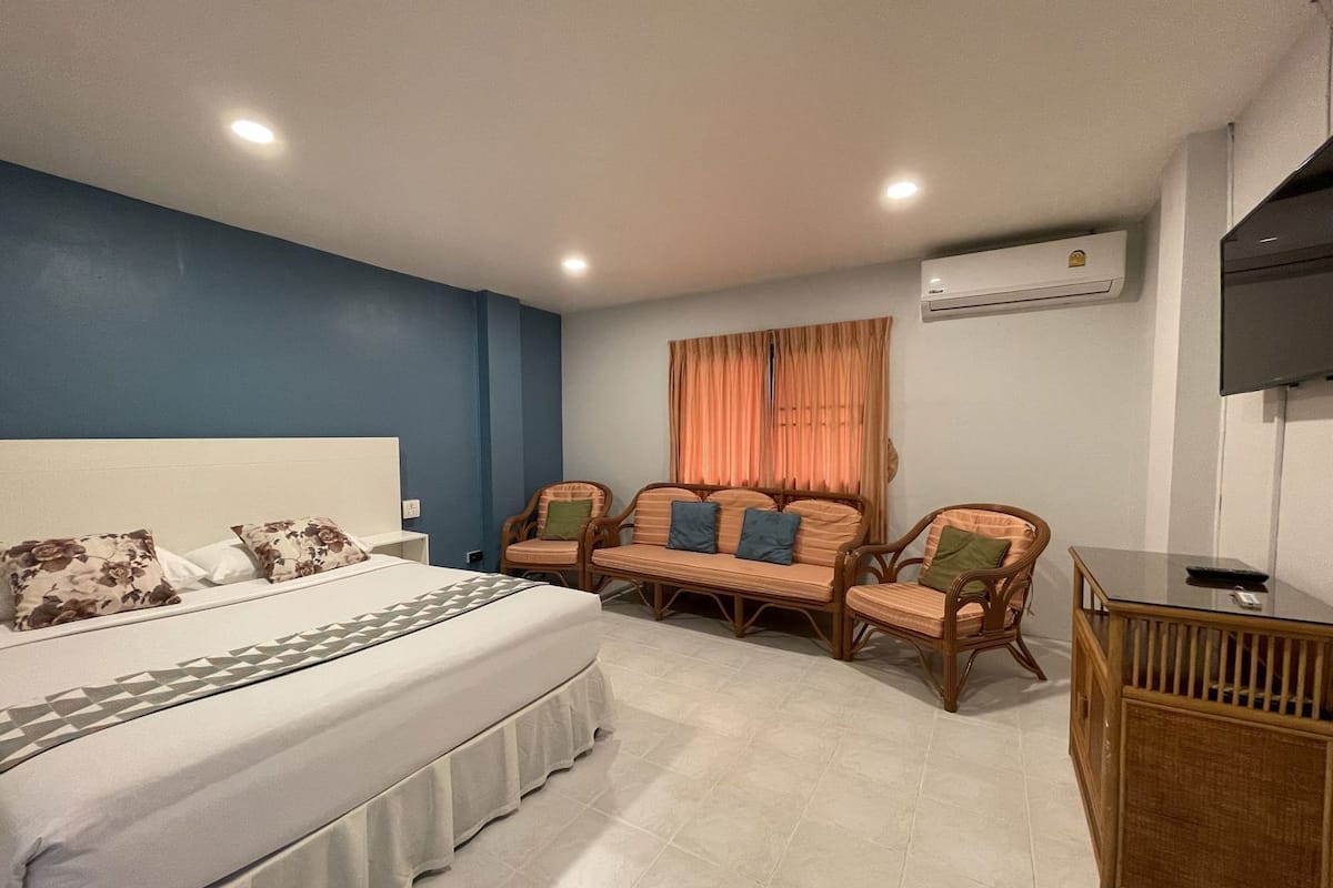 A bedroom with a bed, two chairs, a small table, and an air conditioning unit.