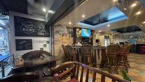 Uma área de bar com móveis de madeira, uma tela de televisão e um aviso sobre happy hour de coquetéis.