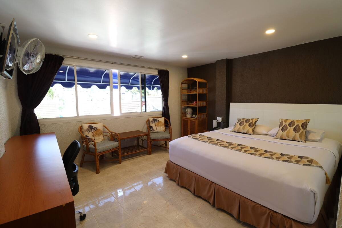 A hotel room with a bed, a desk, a chair, a bookshelf, and a window with curtains.
