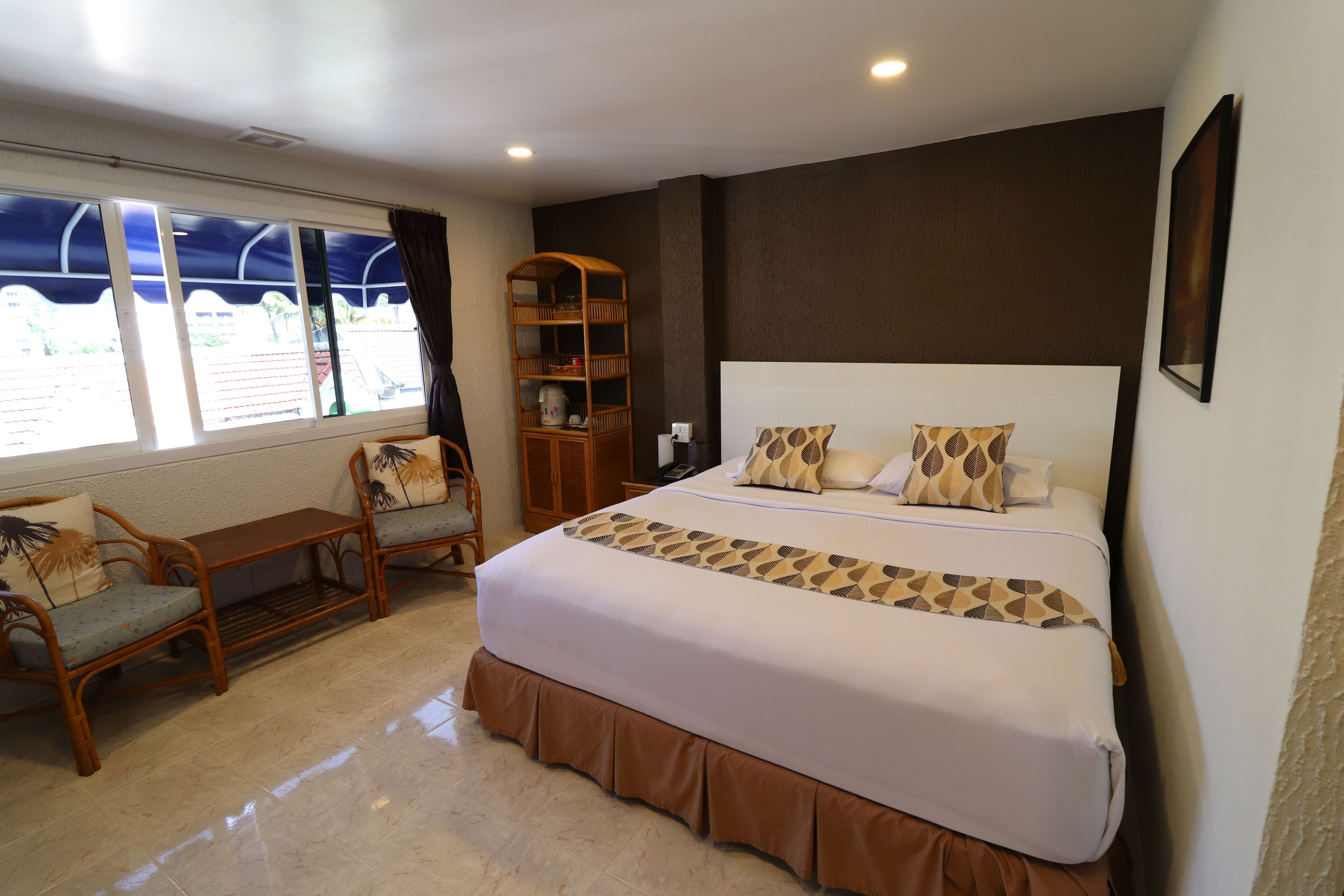 Een slaapkamer met een groot bed, een houten stoel, een klein tafeltje en een boekenplank.