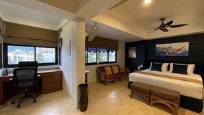 Quarto de hotel com cama, escrivaninha, cadeira e vista para edifícios pela janela.
