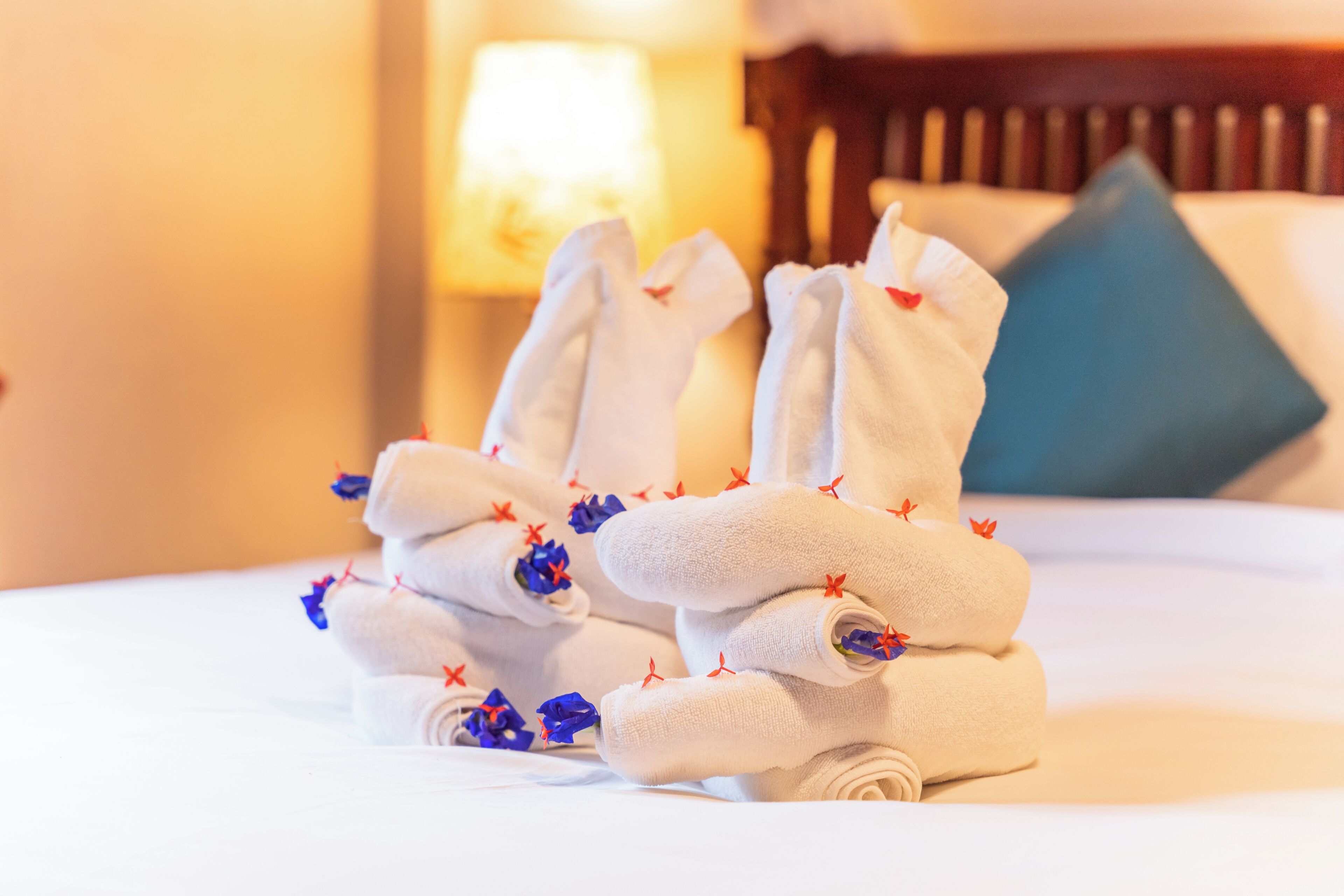 Neatly folded towels with red floral decorations on a bed in a hotel room.