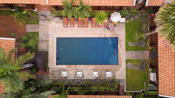 Une vue aérienne d’une piscine entourée de chaises longues, de plantes en pot et d’un chemin en pierre.