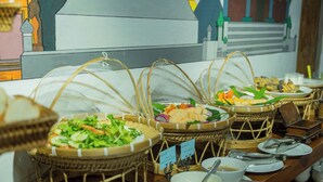 Ein Buffet mit verschiedenen Speisen in Korbflechterarbeiten, umgeben von Tellern, Schüsseln und Besteck.