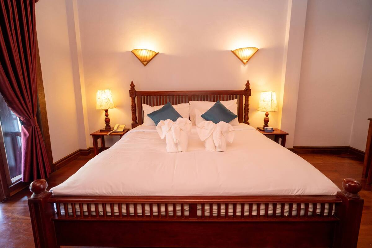 A neatly made bed with white linens and two pillows, a wooden headboard, and two bedside lamps.
