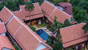 Ein traditionelles Gebäude mit mehreren roten Ziegeldächern, einem zentral gelegenen Pool und umliegender Bepflanzung.