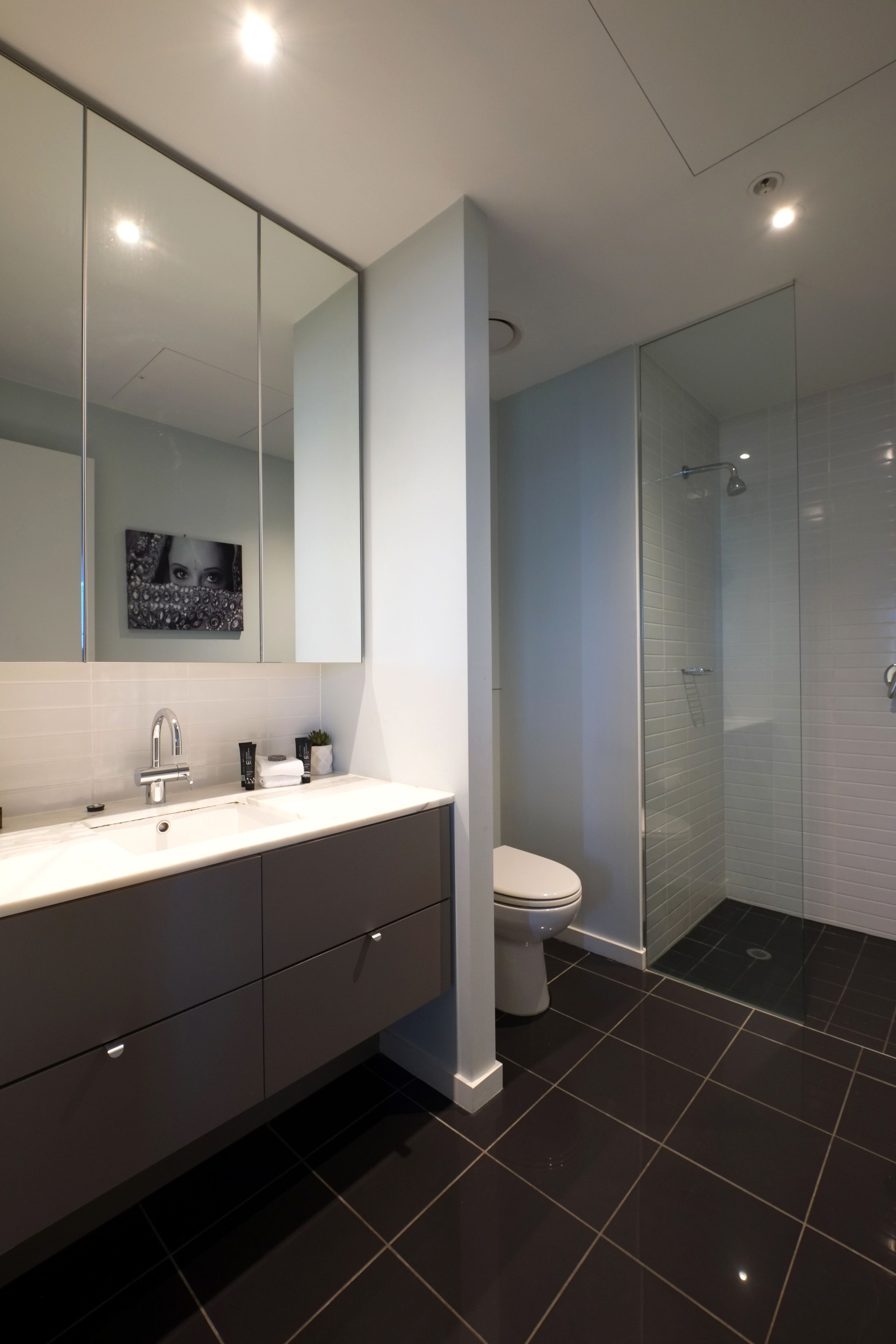 Un baño moderno con un espejo grande, un lavamanos, un inodoro y una ducha con mampara de vidrio.