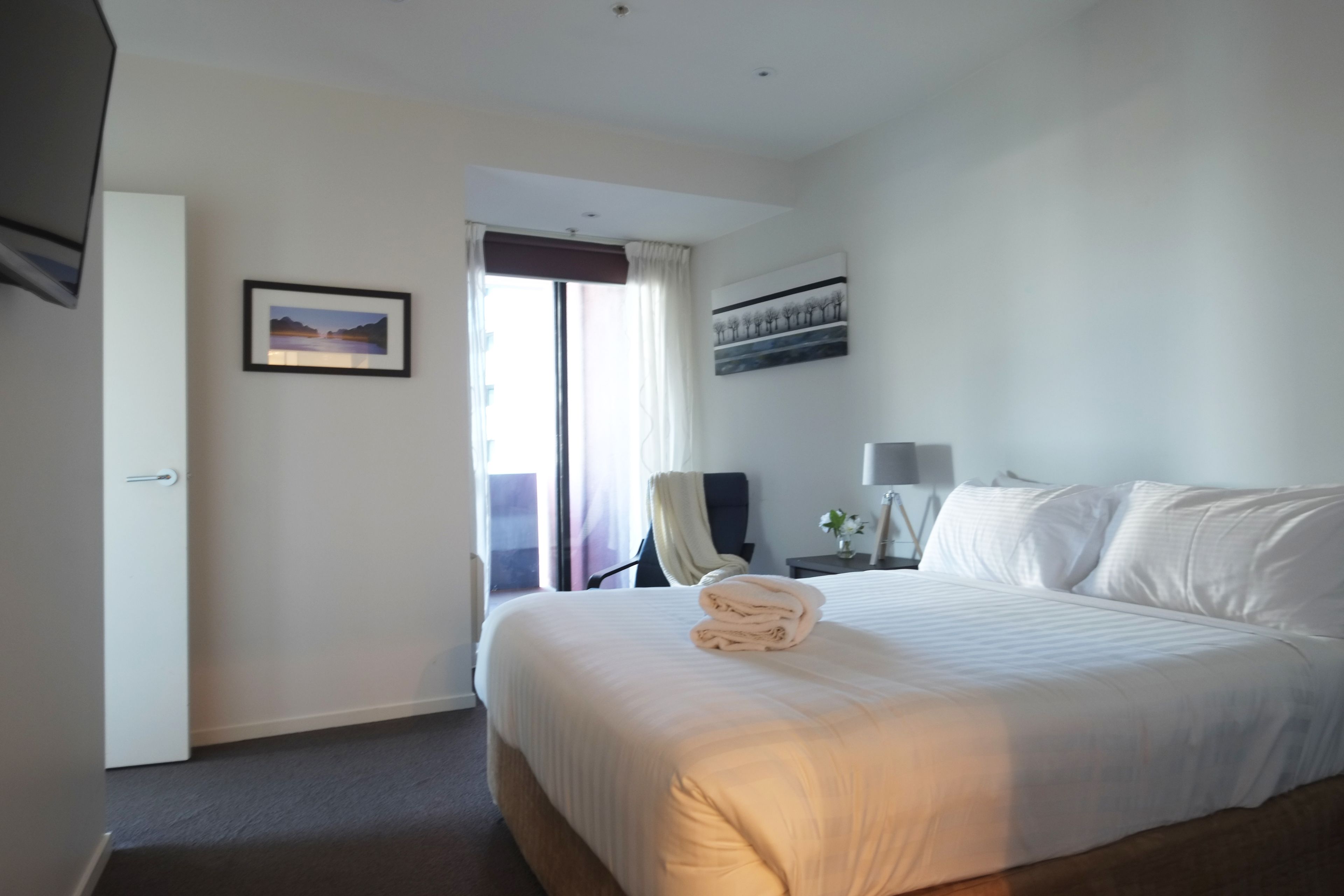 Een hotelkamer met een groot bed, een bureau met lamp, een stoel en een raam met gordijnen.
