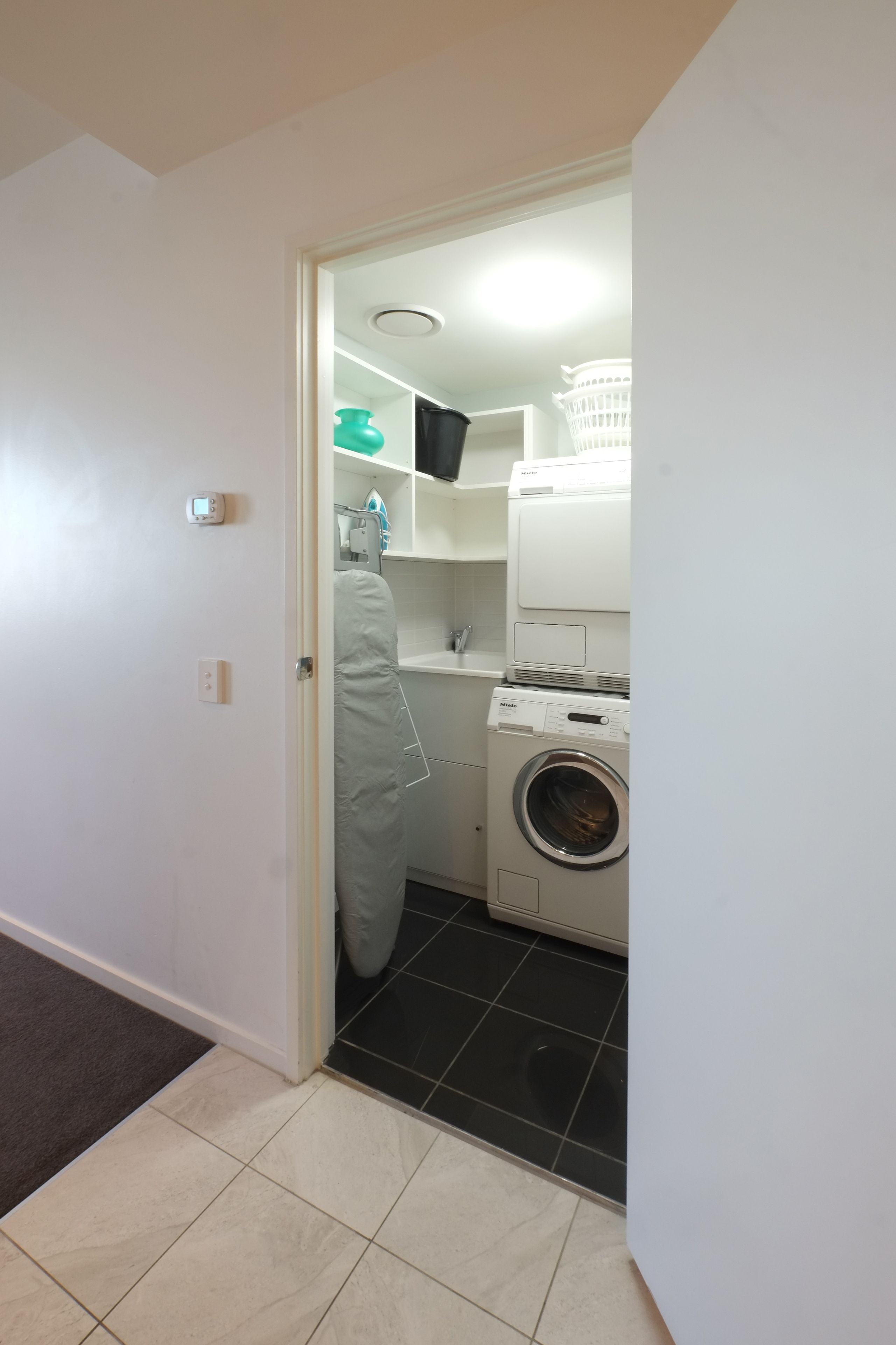 A laundry room with a washing machine, a dryer, and a shelf with a basket.