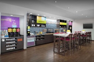Una cafetería moderna con mostrador, taburetes y diversas opciones de café y té.