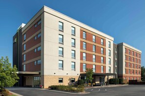 Un hôtel à plusieurs étages au design moderne, caractérisé par un mélange de façades en briques et de couleurs neutres, de grandes fenêtres et un espace d’entrée abrité.