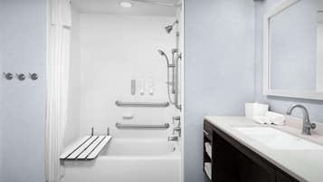 A modern bathroom with a bathtub, shower, and sink. It includes grab bars, a towel rack, and a mirror.