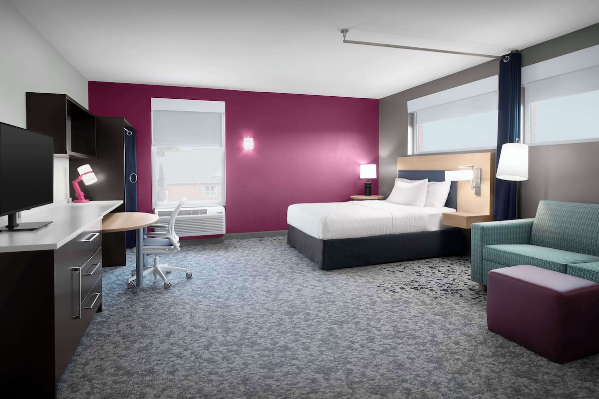A hotel room with a bed, a desk, a chair, a sofa, and a TV.