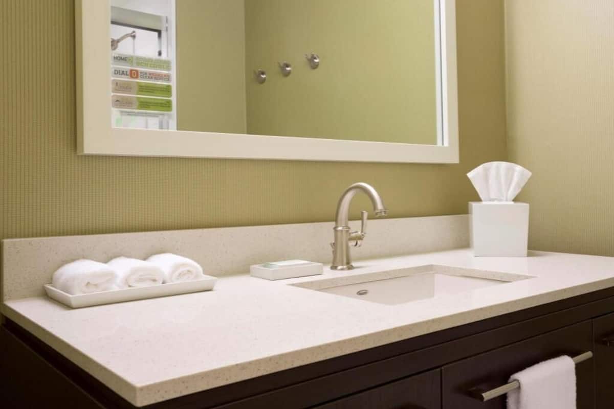 A bathroom with a sink, mirror, towel rack, and a tissue box.