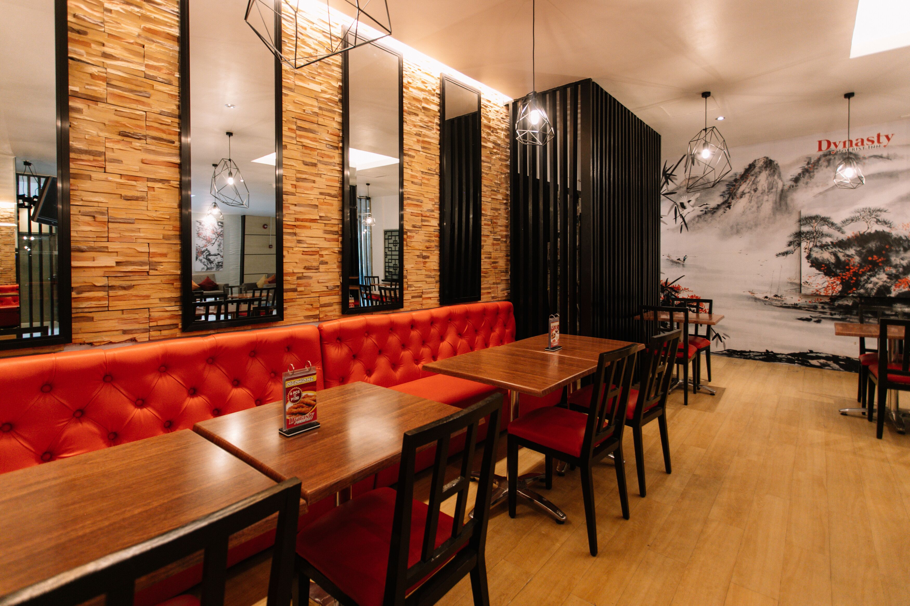 A restaurant interior with wooden walls, red cushioned seating, and a mural depicting a mountainous landscape.