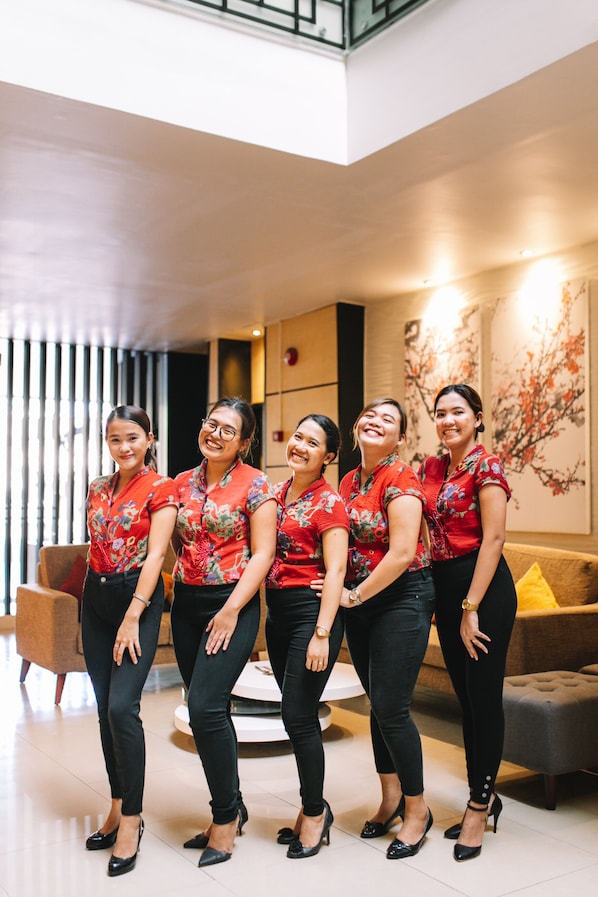 A group of five individuals in matching red floral shirts and black pants standing in a modern indoor setting with a sofa and a decorative wall piece.