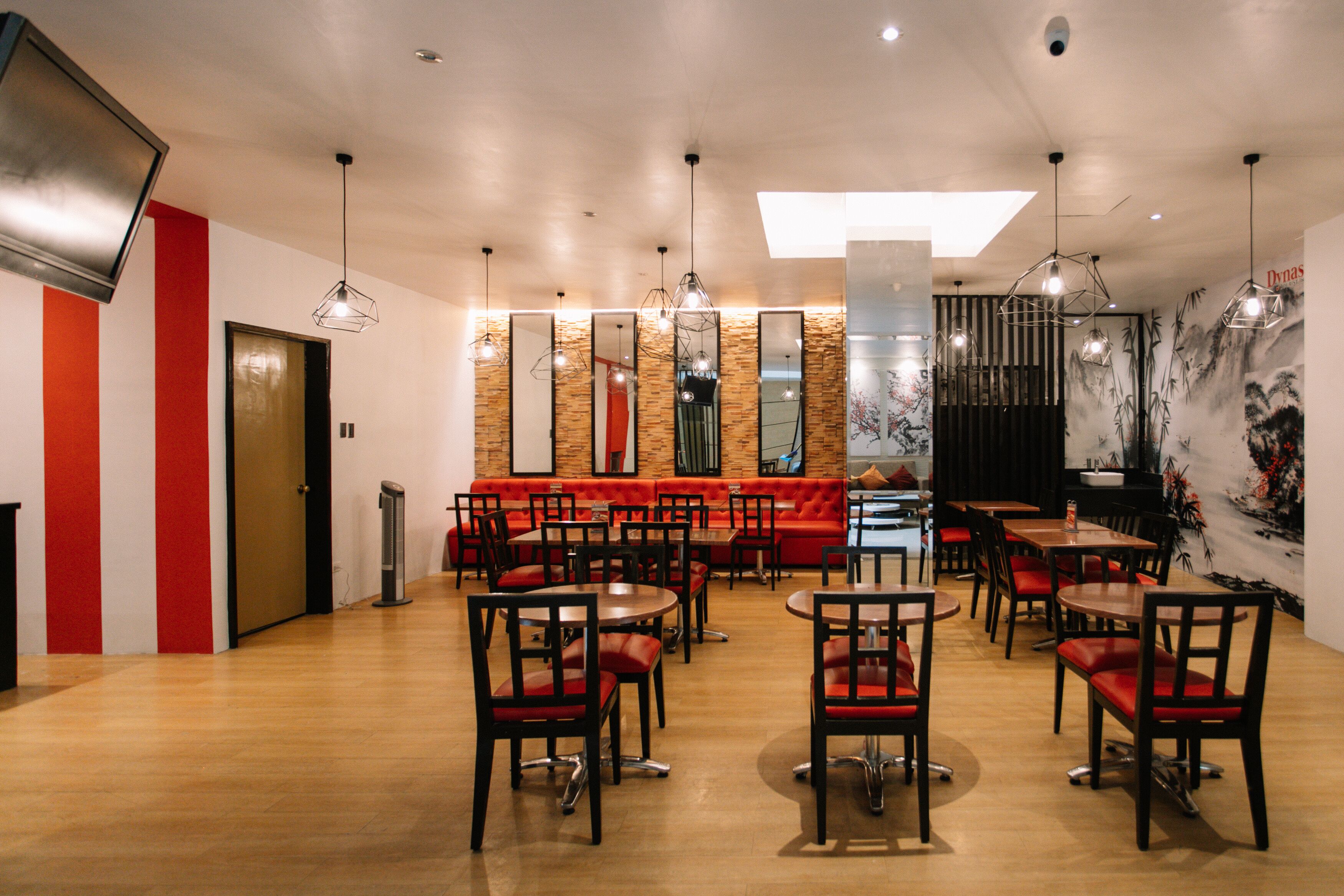 A restaurant with wooden flooring, red and white decor, and multiple dining tables and chairs.