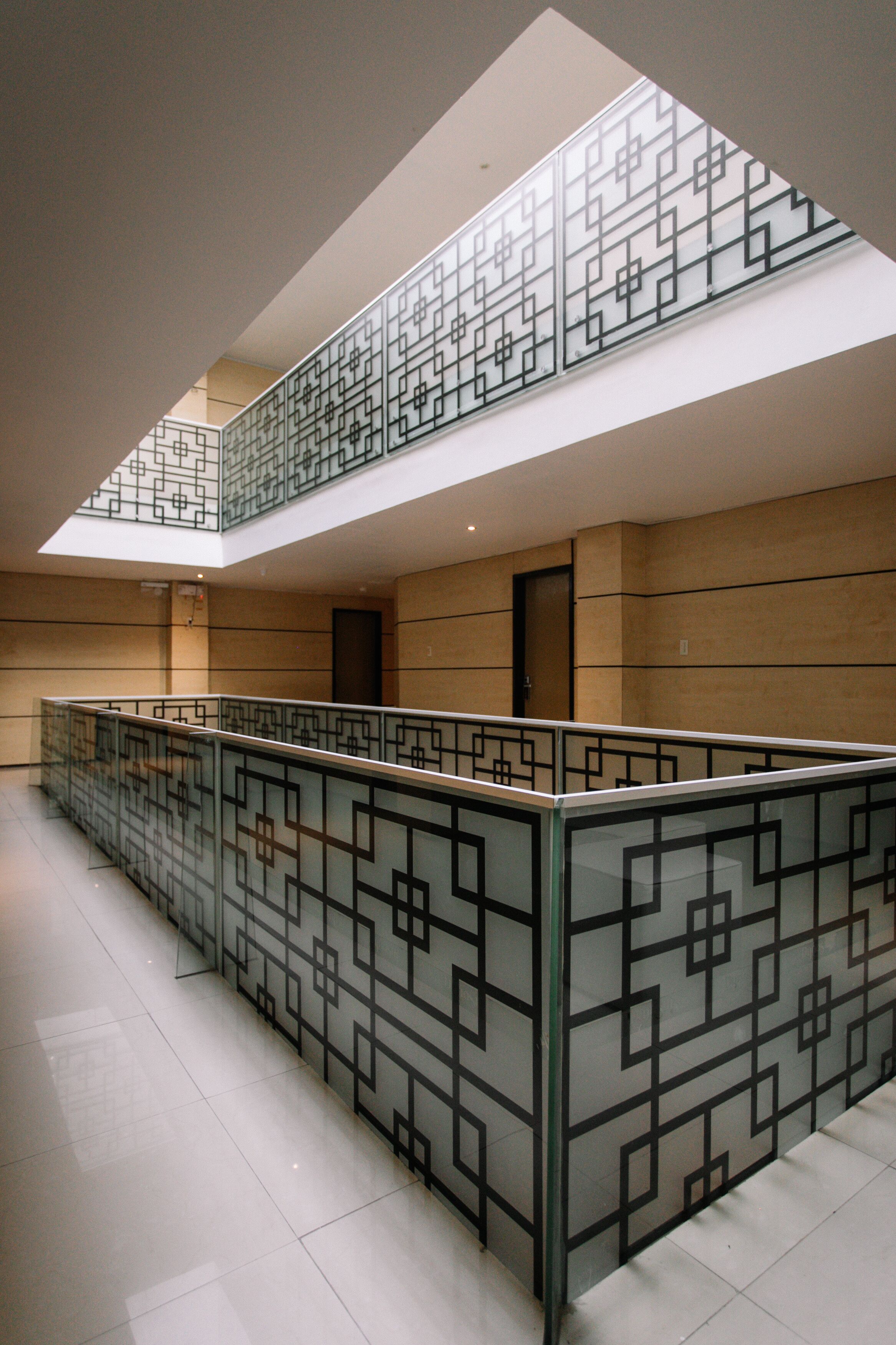 A modern interior with a glass railing and geometric patterns, a second-floor balcony, and a door on the ground floor.