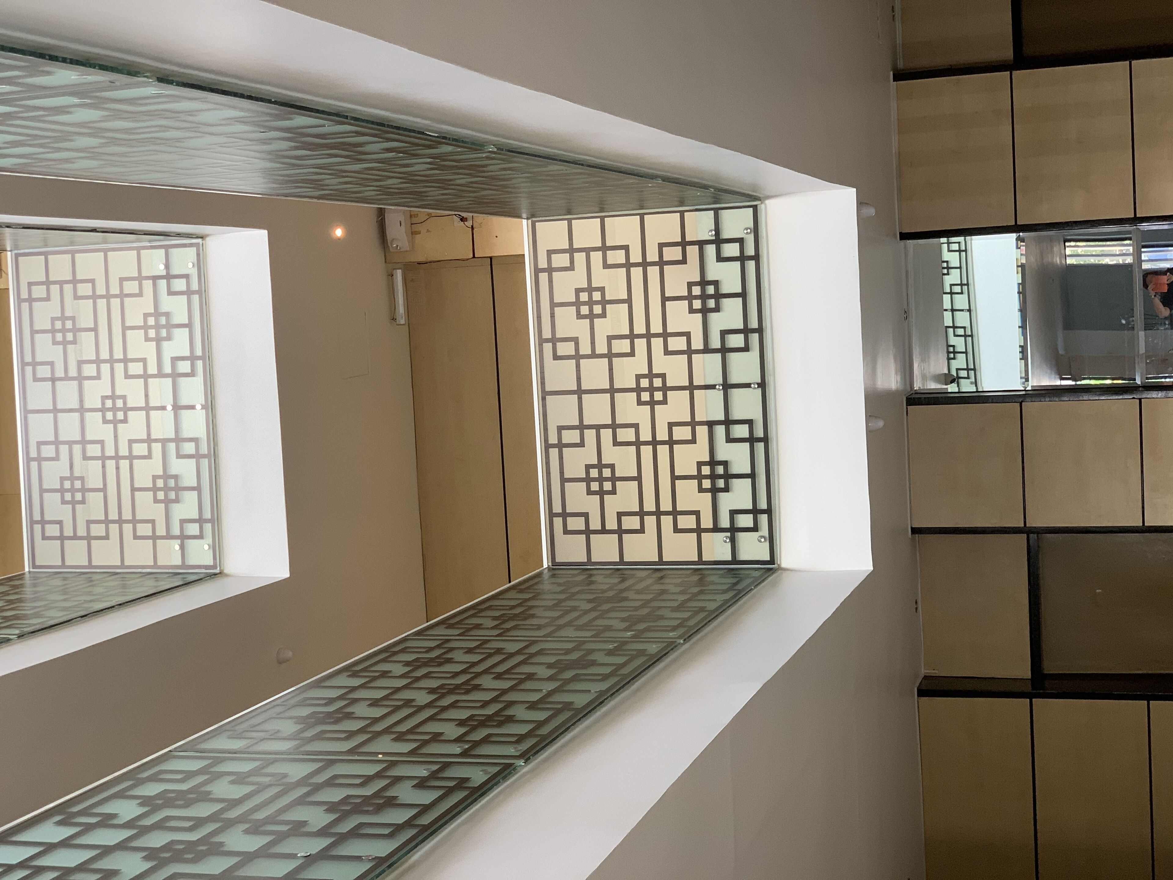 Un interior moderno con un separador de vidrio que presenta patrones geométricos, suelo de baldosas y una pared blanca con un hueco empotrado.