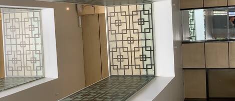 Un interior moderno con un separador de vidrio que presenta patrones geométricos, suelo de baldosas y una pared blanca con un hueco empotrado.