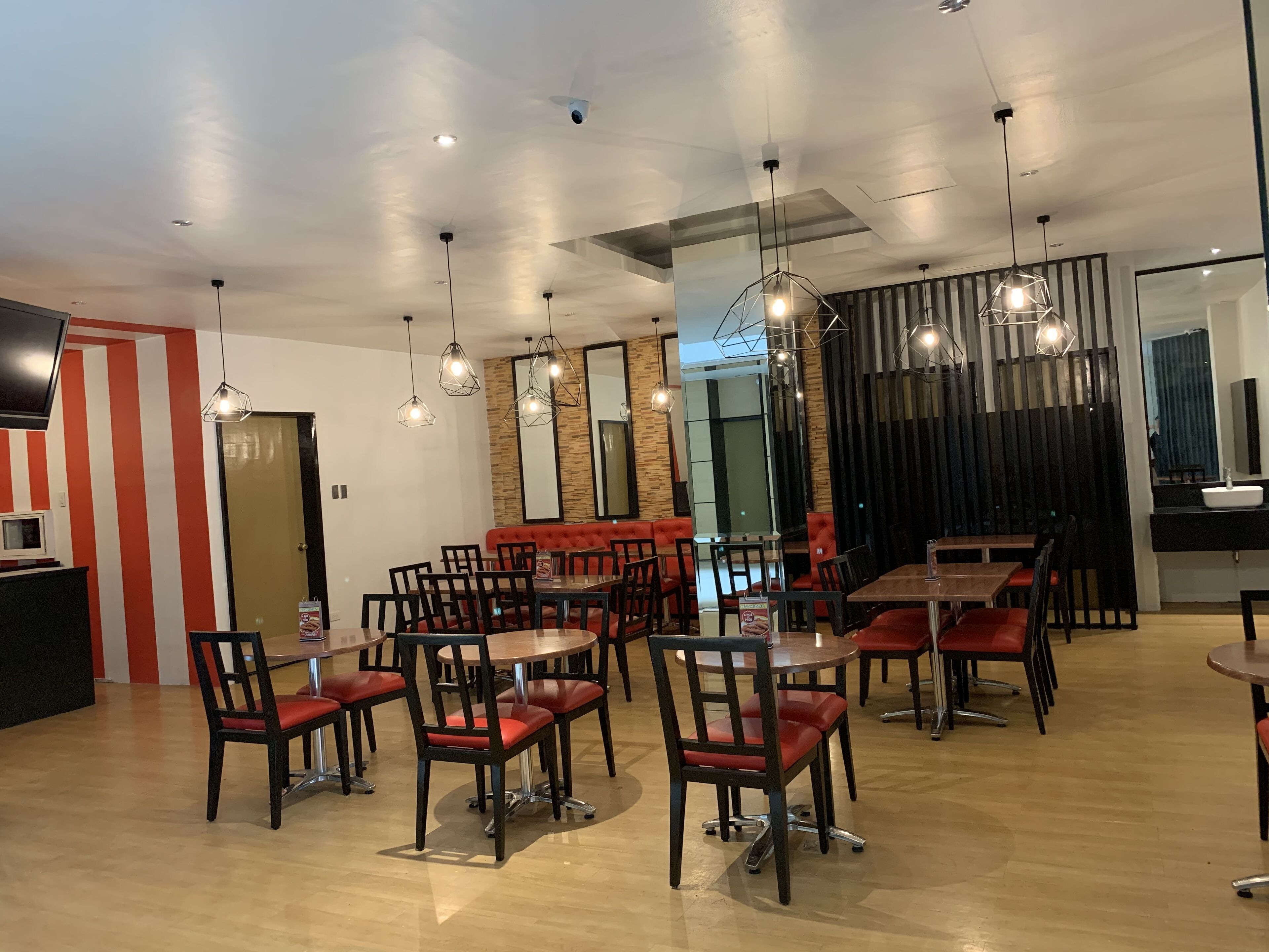 Uma área de jantar moderna com várias mesas e cadeiras, um espelho grande e iluminação pendente.