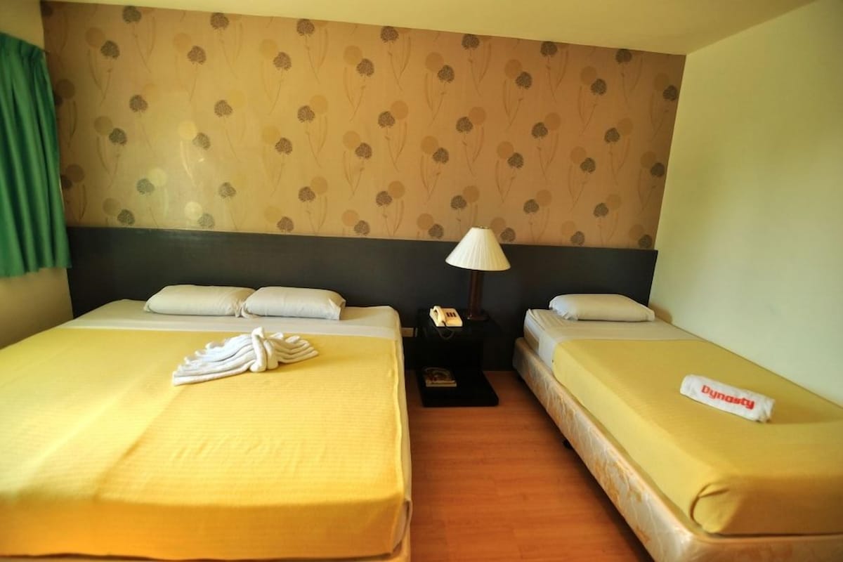 Ein Hotelzimmer mit zwei Betten, einem Nachttisch mit Lampe und einer Wand mit floralem Muster.