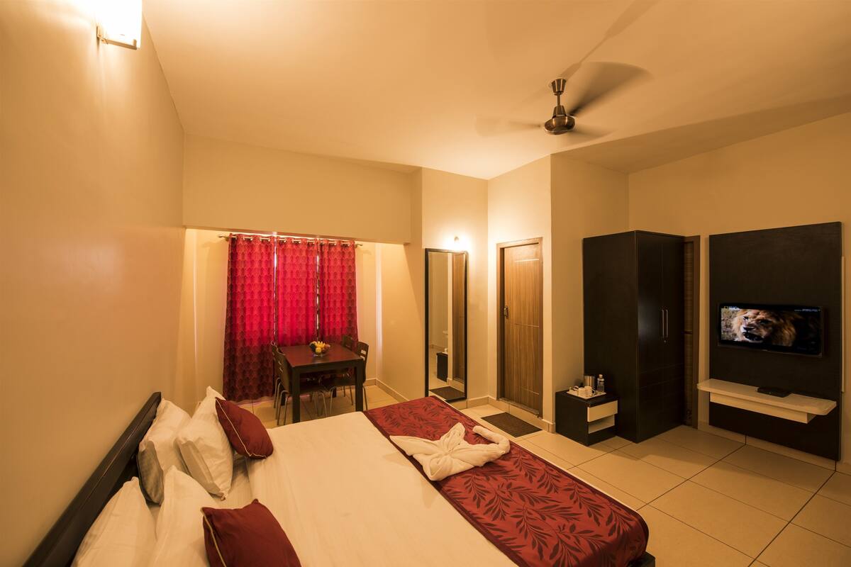 Habitación de hotel con cama, escritorio, silla, televisor y armario.