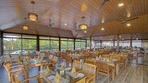 Un comedor amplio con varias mesas y sillas, ventanas grandes que ofrecen vistas al exterior y ventiladores de techo.