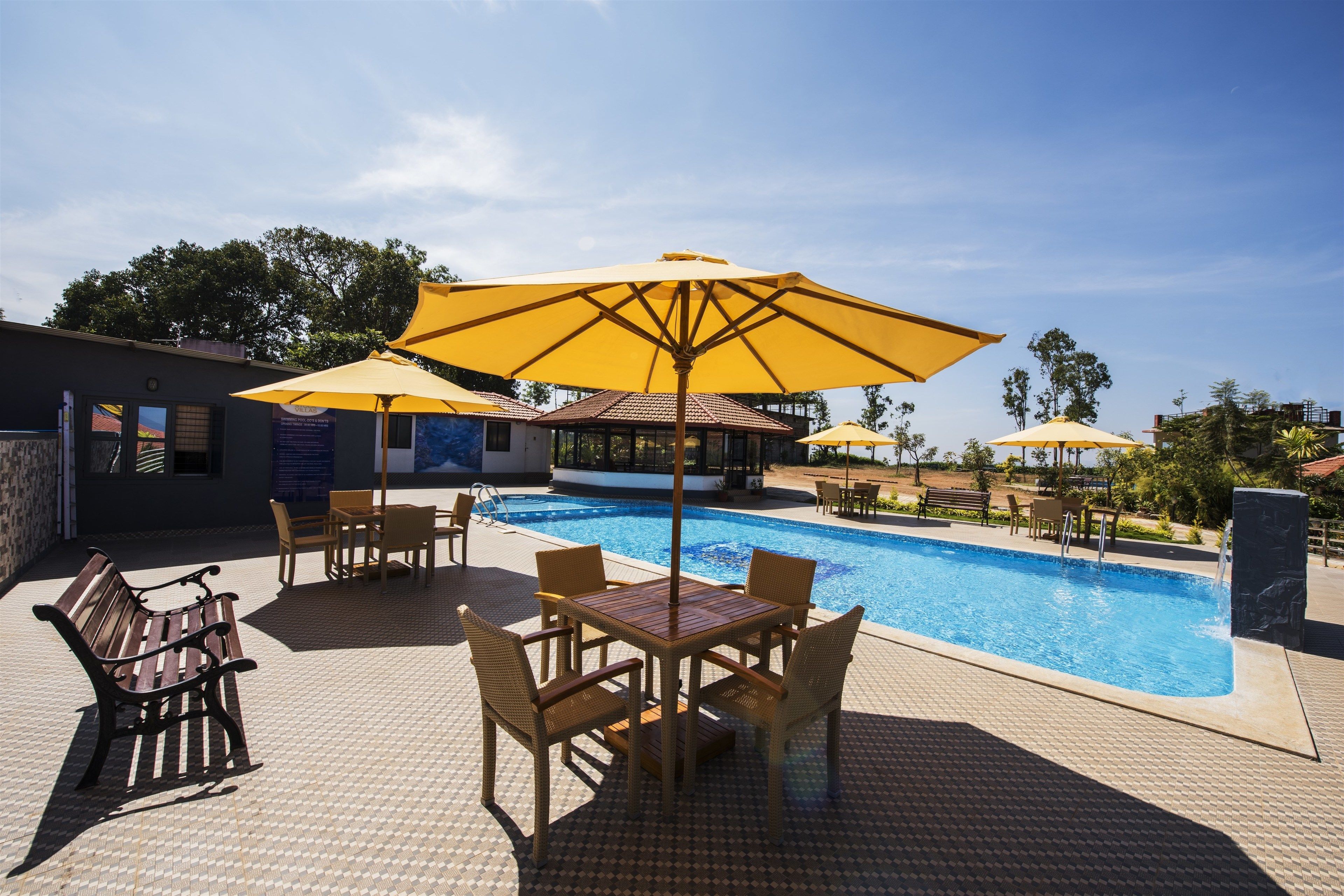 Zona junto a la piscina con solárium de baldosas, sillas reclinables de madera y sombrillas amarillas.