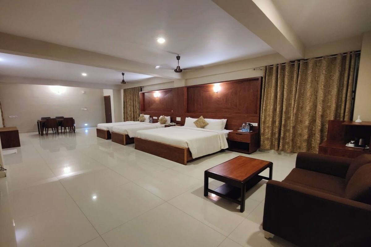 Habitación de hotel con dos camas, un sofá, una mesa de centro, una televisión y un área de comedor con sillas.